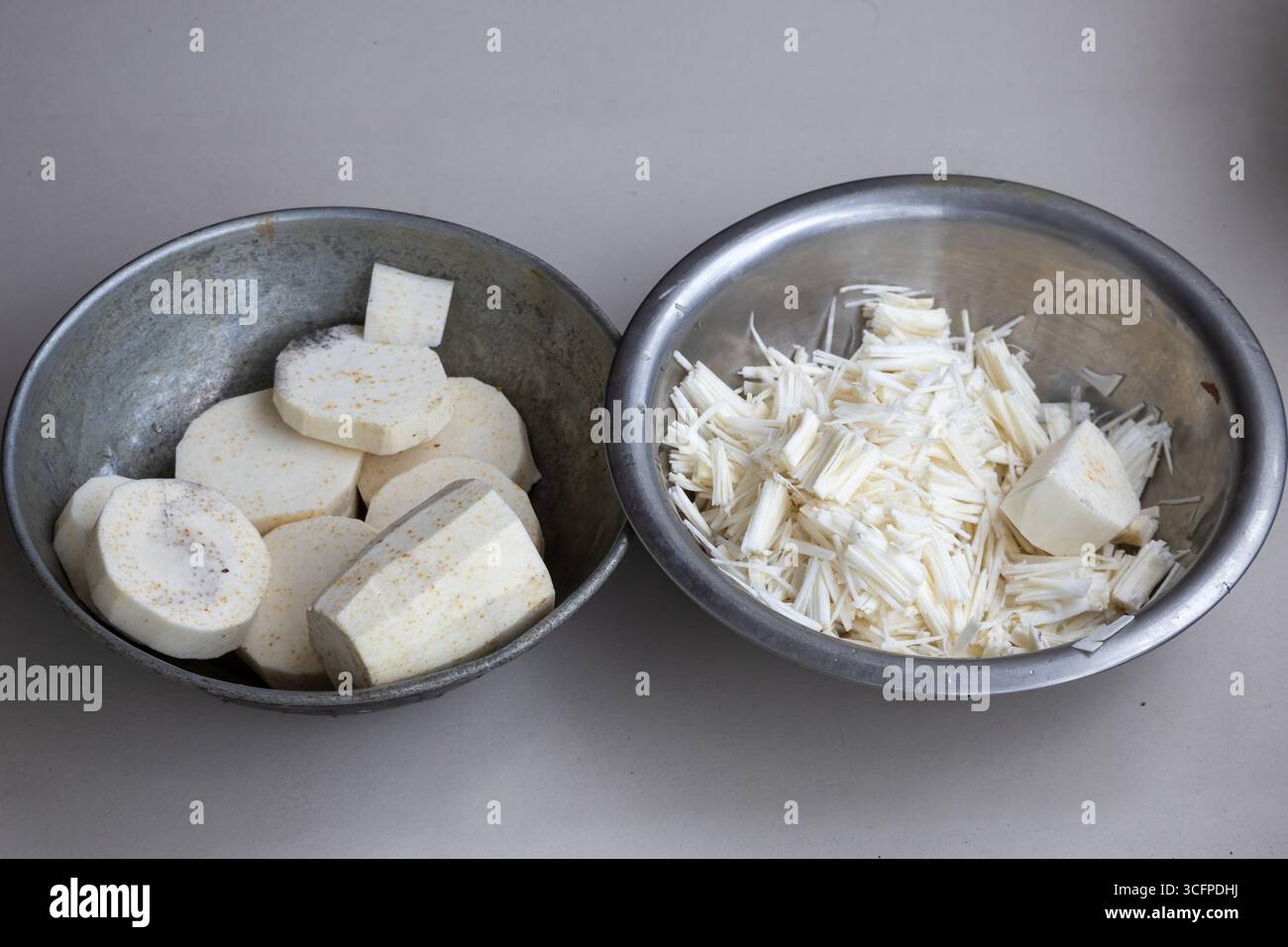 Taro crudo (colocasia esculenta) fette di verdure e taro grattugiato in un recipiente, pronto per la cottura. Preparazione sana e commestibile delle radici in cucina. Foto Stock