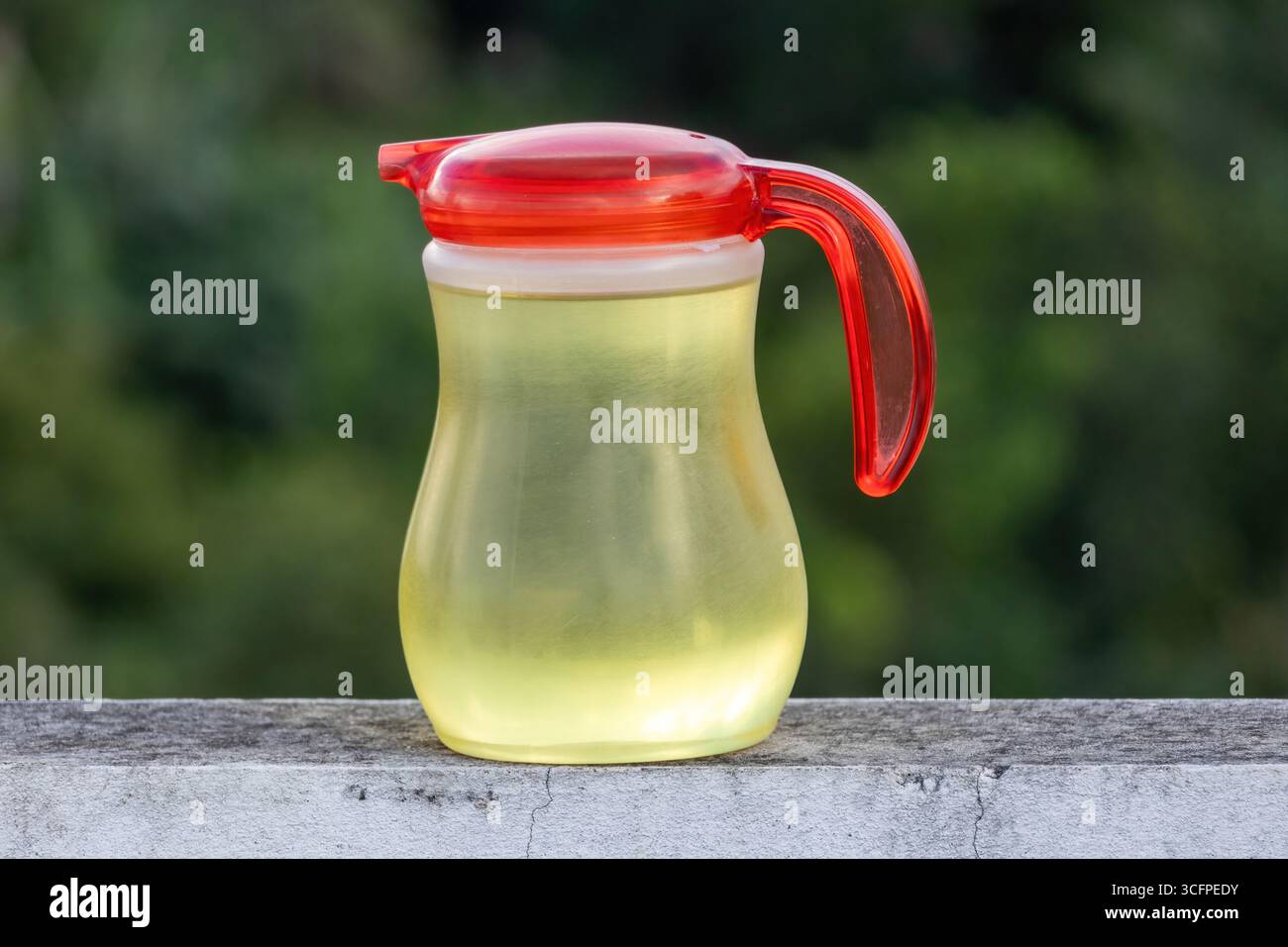 Primo piano di un vaso di plastica riempito con olio di soia dorato, appoggiato su una parete rustica e intemprata con uno sfondo naturale e leggermente sfocato. Foto Stock