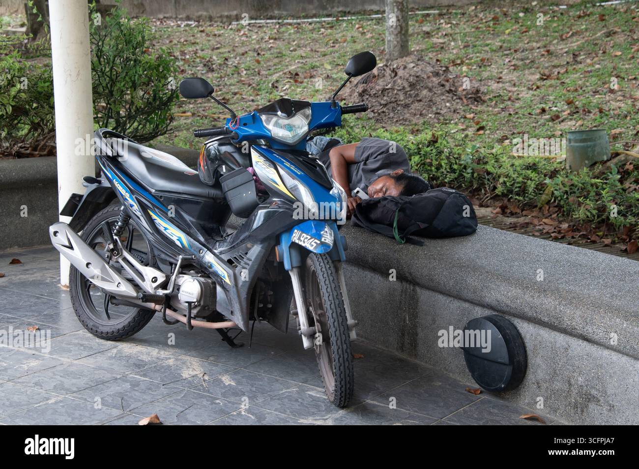 Un giovane fa un pisolino pomeridiano accanto alla sua moto in un parco a Kuala Lumper in Malesia Foto Stock