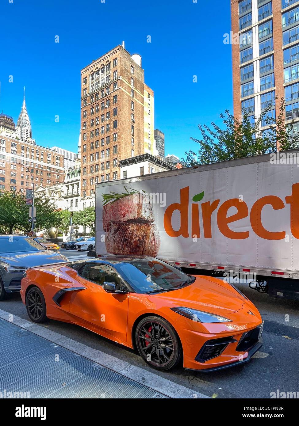 Divertente scena di strada di una superveloce Corvette parcheggiata accanto a un enorme furgone diretto a Midtown Manhattan, 2025, New York City, Stati Uniti - Immagine stock catturata con smartphone