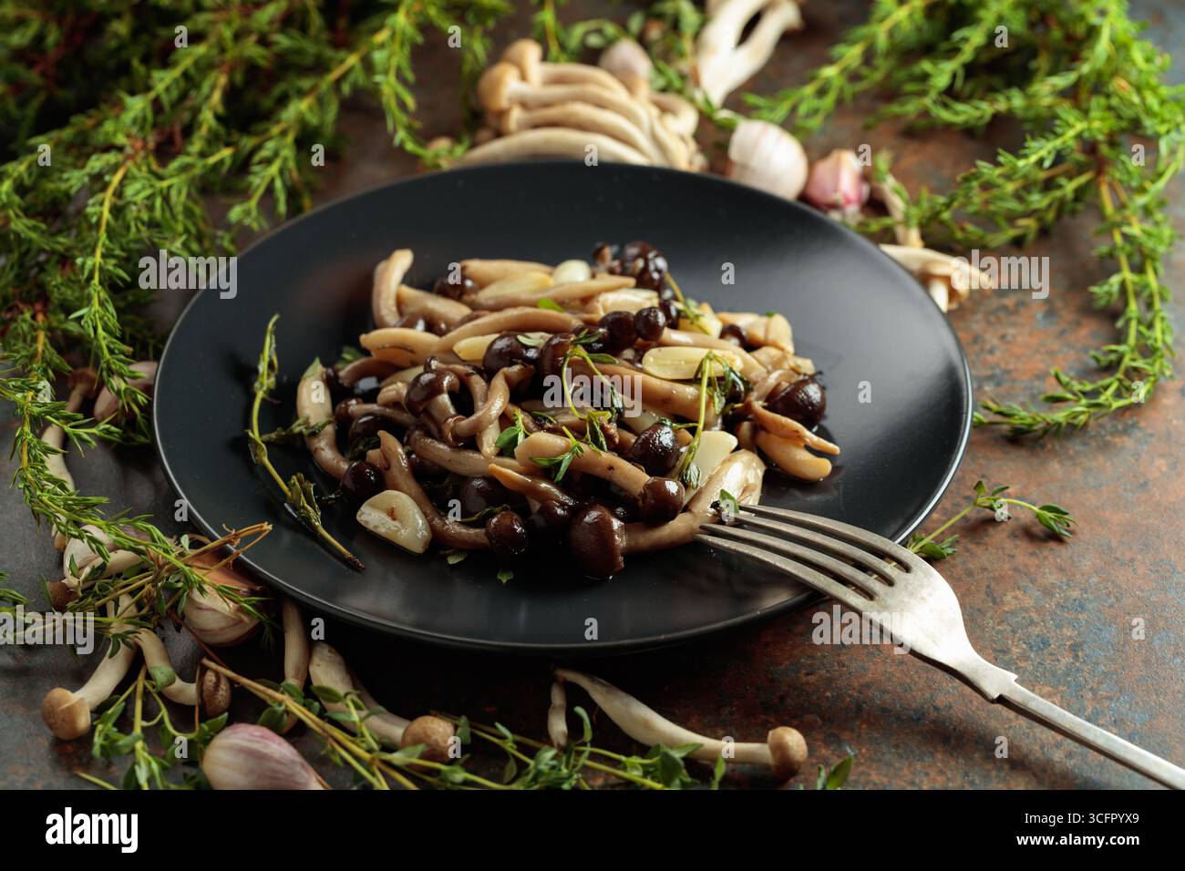 Shimeji fritti con timo e aglio su un piatto nero. Funghi freschi e preparati con ingredienti. Cucina tradizionale giapponese. Foto Stock
