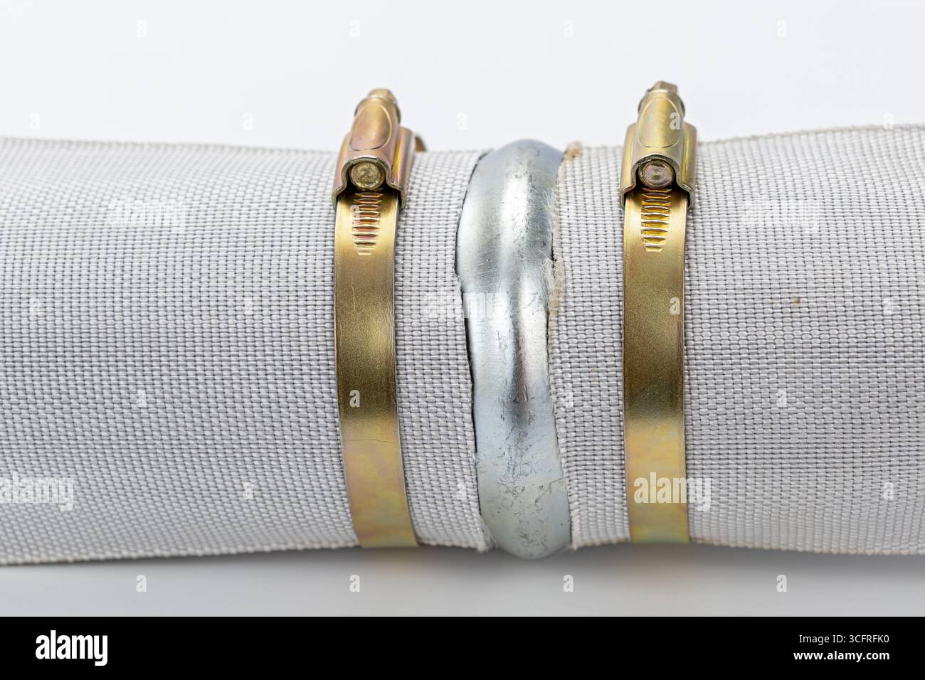 Un connettore per tubi in metallo con fascetta in ottone, tubo flessibile in tessuto bianco, raccordo industriale, collegamento sicuro, sfondo pulito Foto Stock