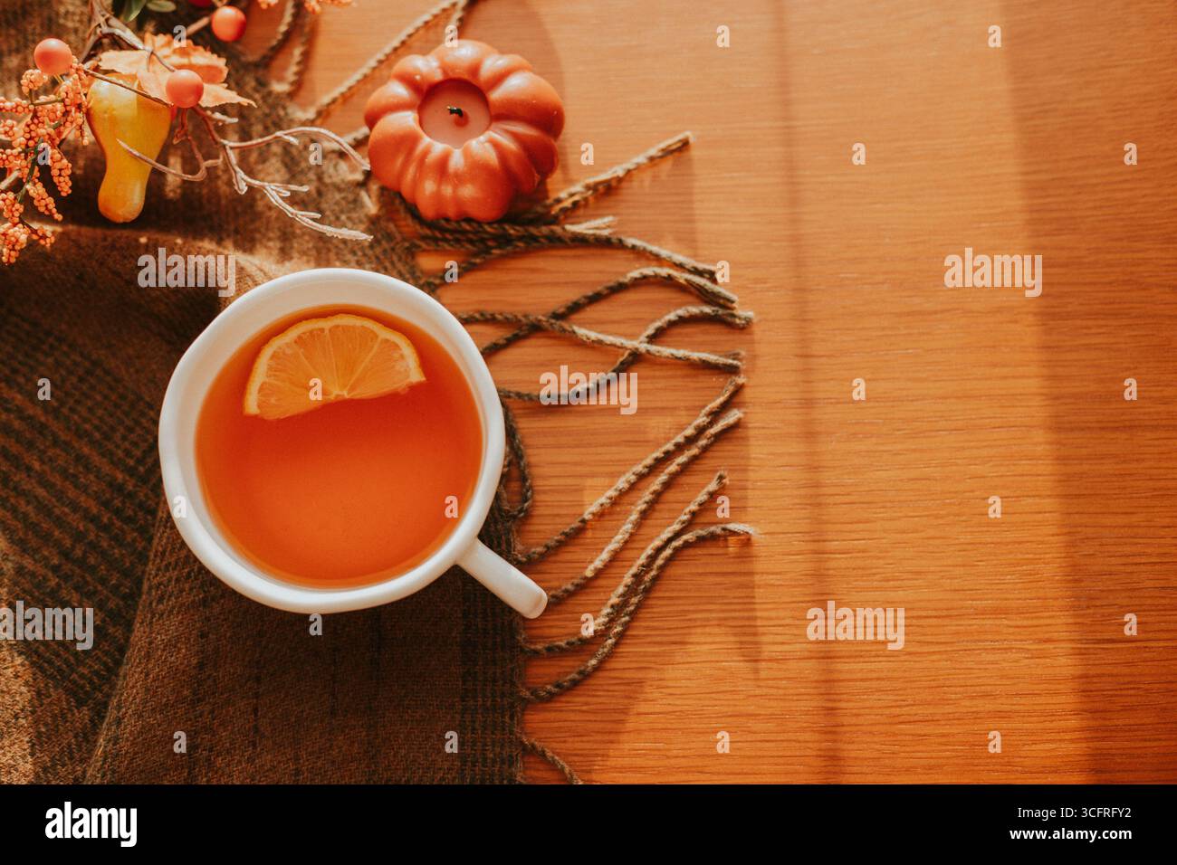 Un tè caldo servito in una tazza bianca con una fetta di limone, circondato da un'accogliente disposizione autunnale con piccole zucche, foglie e texture rustiche Foto Stock