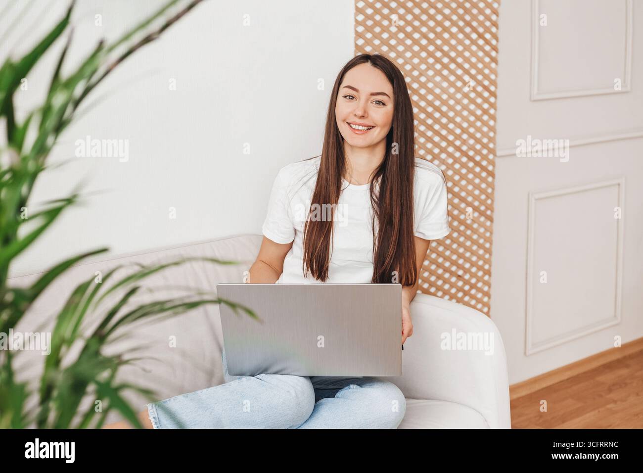 Una giovane designer di interni è seduta sul divano con un laptop che guarda la fotocamera Foto Stock