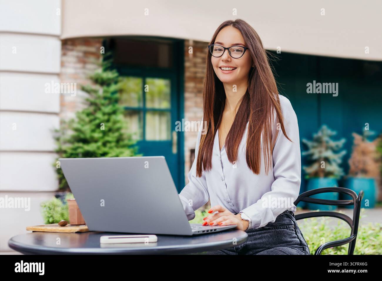 La studentessa si siede al tavolo di un bar, usa un computer portatile e guarda la fotocamera. Cerca lavoro remoto, posti vacanti. Responsabile risorse umane Foto Stock