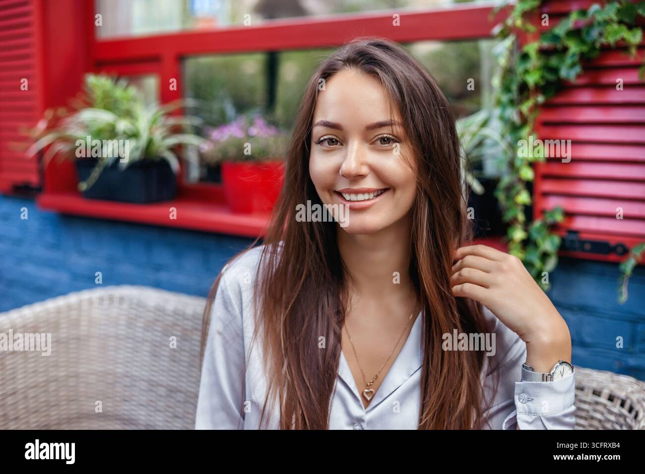 Ritratto ravvicinato della giovane donna ucraina che sorride e siede all'aperto sulla terrazza del caffè con sfondo verde di piante. Attività e modalità festività Foto Stock
