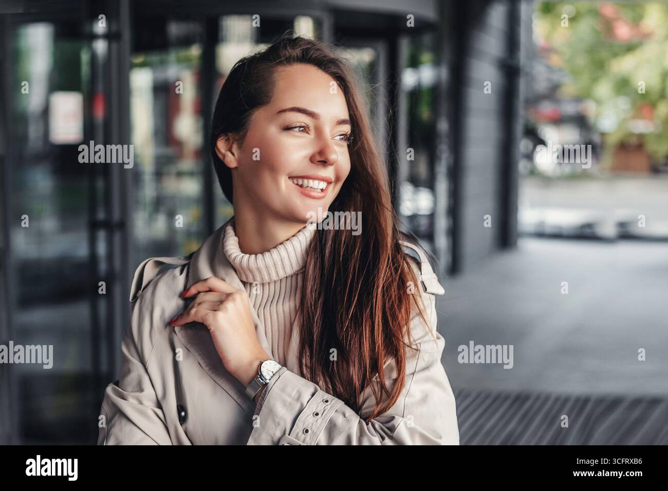 Ritratto di una giovane donna felice sullo sfondo di un edificio di uffici con indosso un trench. copia spazio Foto Stock
