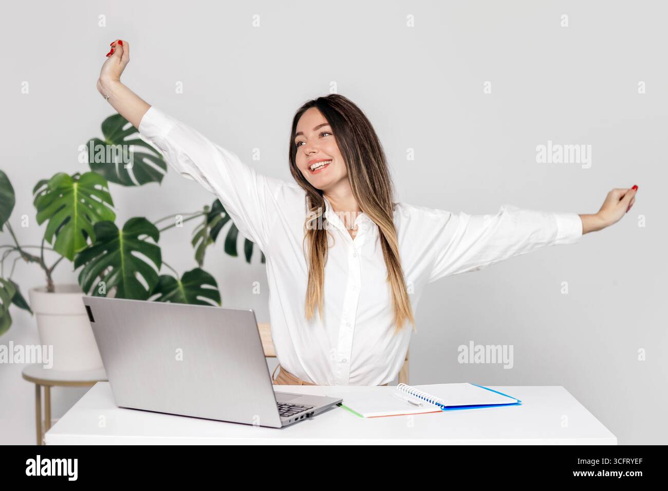Giovane donna d'affari che si allunga le braccia seduta alla scrivania. Una ragazza fa esercizi fisici durante una pausa di lavoro. Psicologia dei dipendenti aziendali Foto Stock