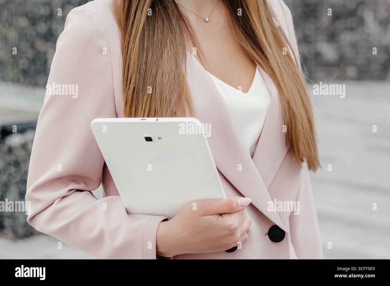 Felice donna d'affari caucasica in una tuta da lavoro beige sorridente tenendo in mano un tablet e guardando lontano. Marketing su Internet, analista finanziario, Foto Stock