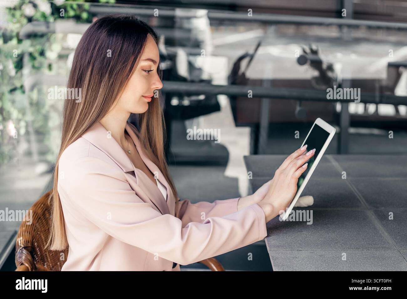 vista del profilo di una giovane donna d'affari seduta a un tavolo in un bar con un tablet. Donna manager, analista, consulente aziendale, marketer Foto Stock