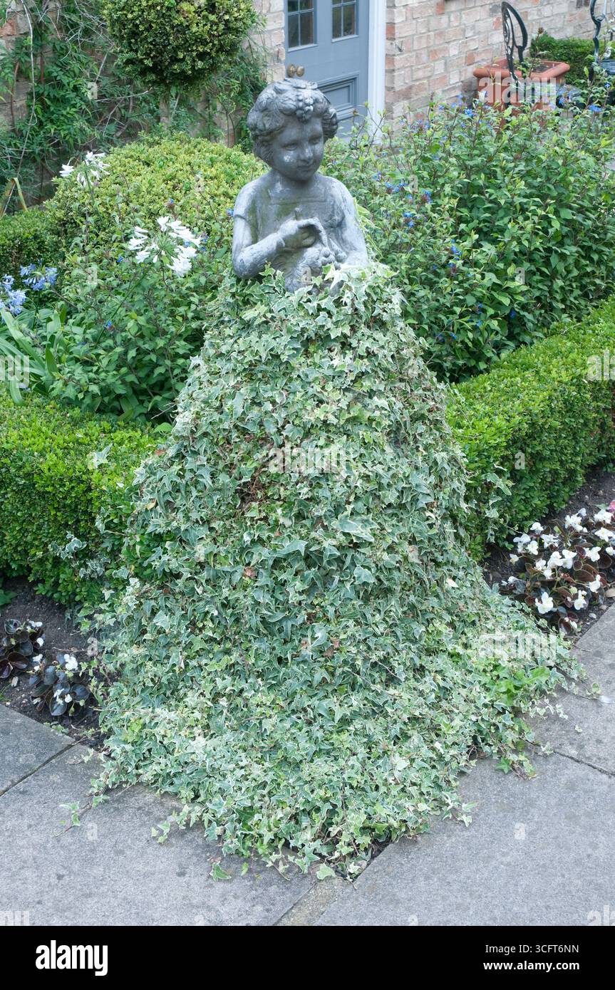Un incantevole giardino presenta una statua di una ragazza circondata da lussureggiante vegetazione, creando una scena stravagante piena di fiori vibranti. Foto Stock