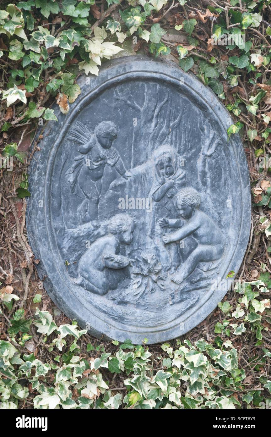 Una scultura in rilievo raffigura bambini impegnati in attività ludiche con la natura, circondati da vibranti edera verde e alberi. Foto Stock