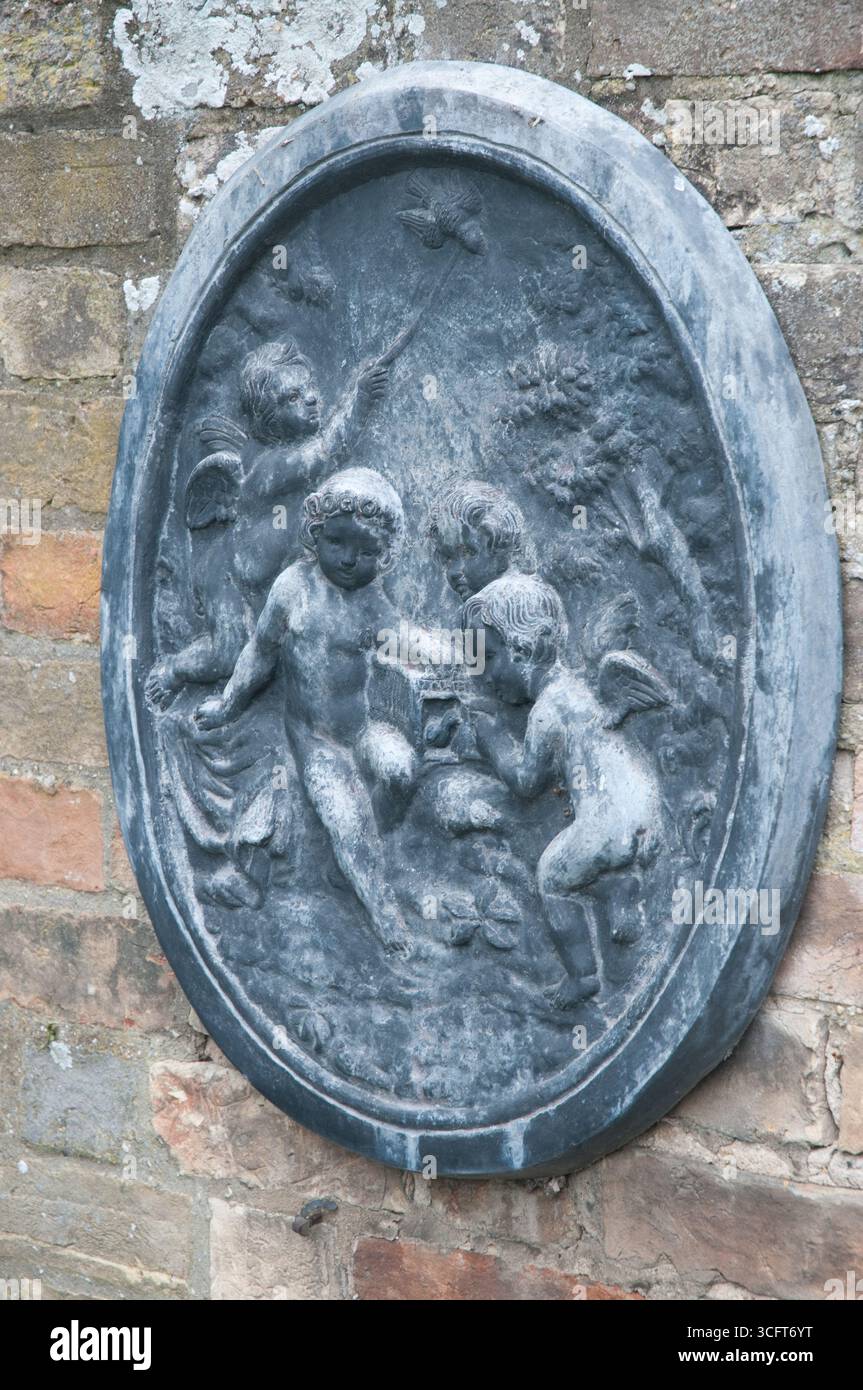 Quattro cherubini interagiscono con elementi naturali in una dettagliata scultura a bassorilievo montata su un muro rustico in pietra. Foto Stock