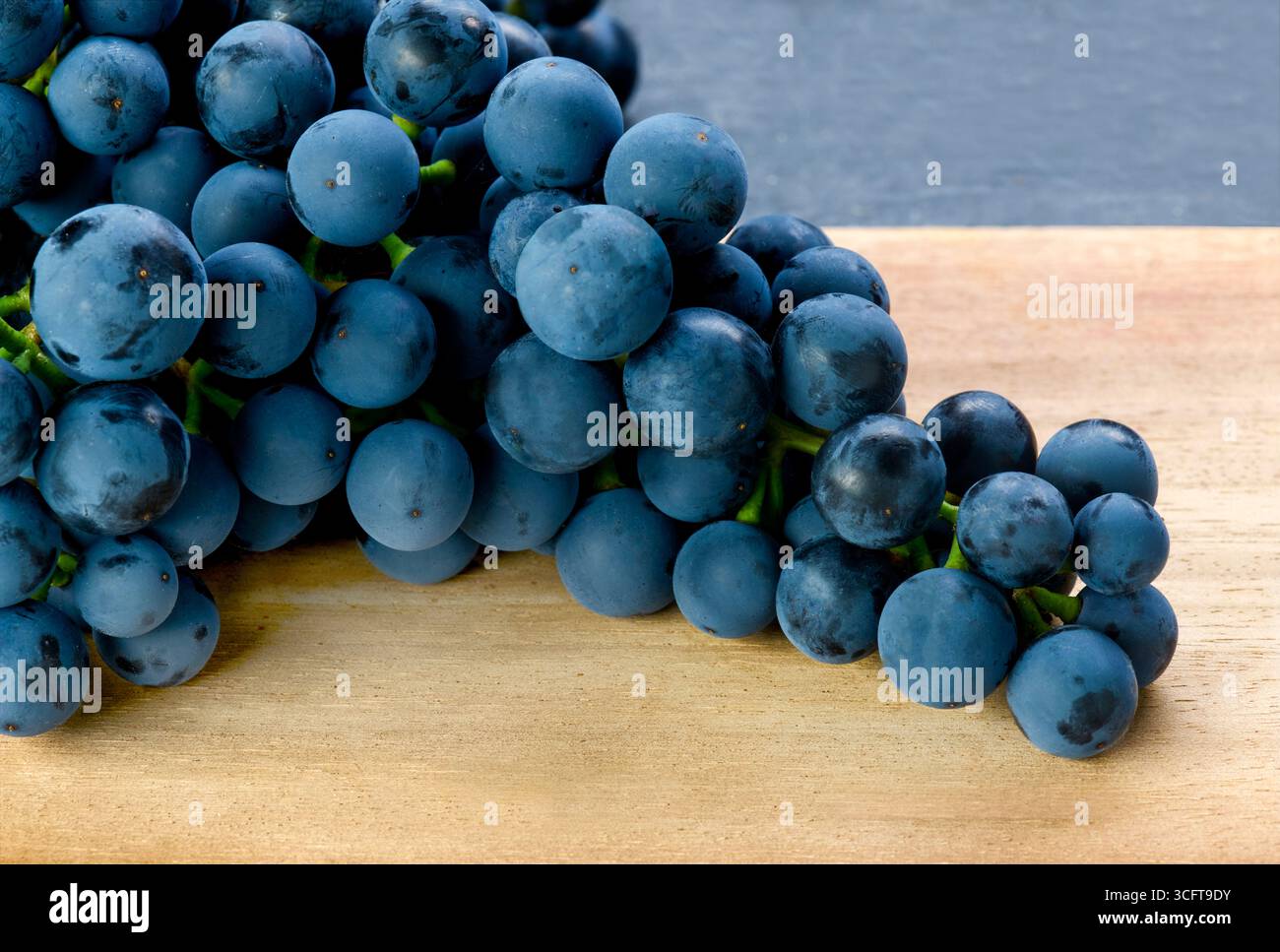 Primo piano di un mucchio di uve scure biologiche fresche su una superficie in legno, ideale per il cibo, la raccolta e i temi della frutta naturale. copiare lo spazio a destra Foto Stock