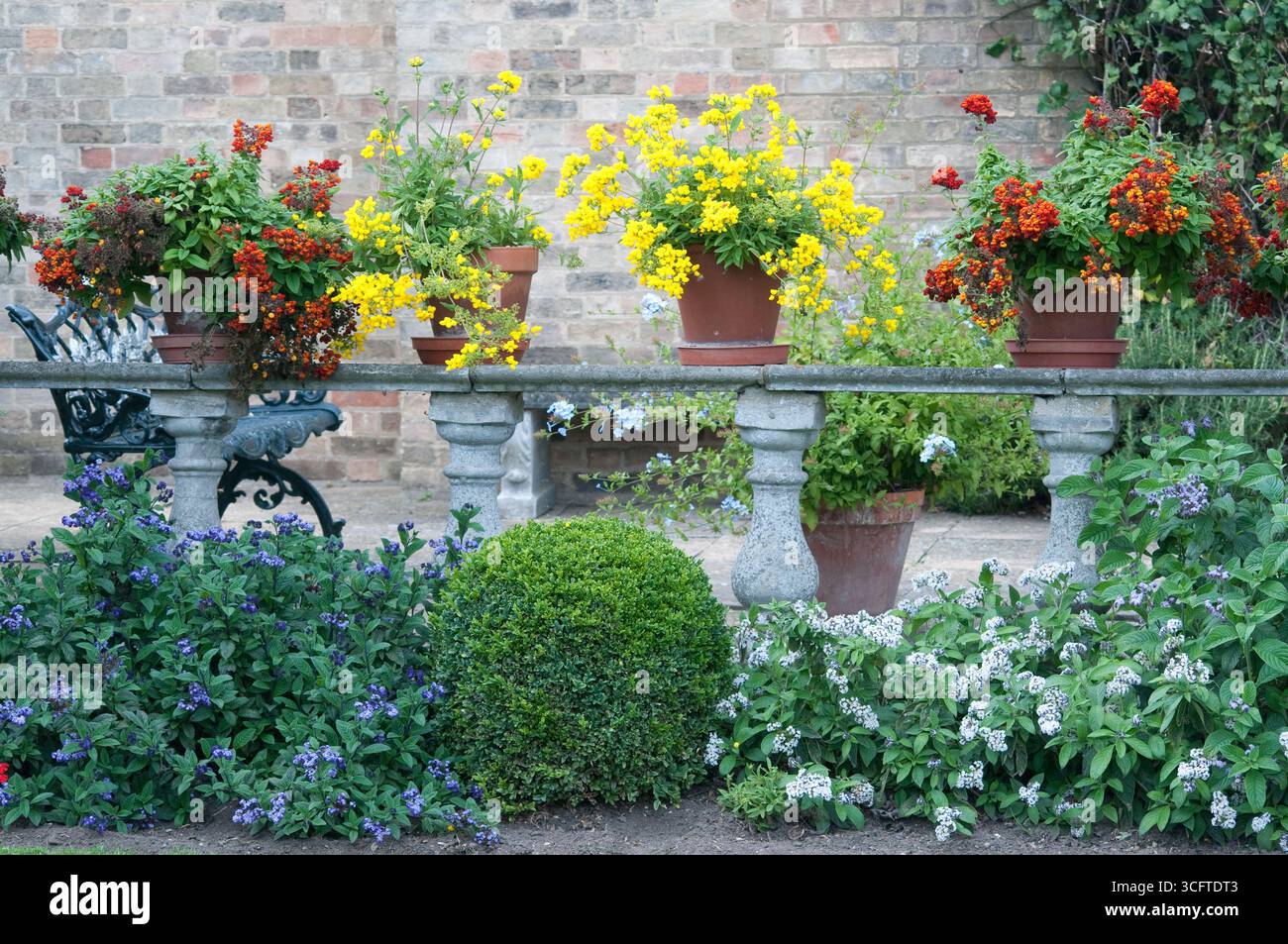 Vasi di fiori dai colori vivaci traboccano di fiori, dando vita a un giardino sereno con vegetazione lussureggiante e accenti di pietra. Foto Stock