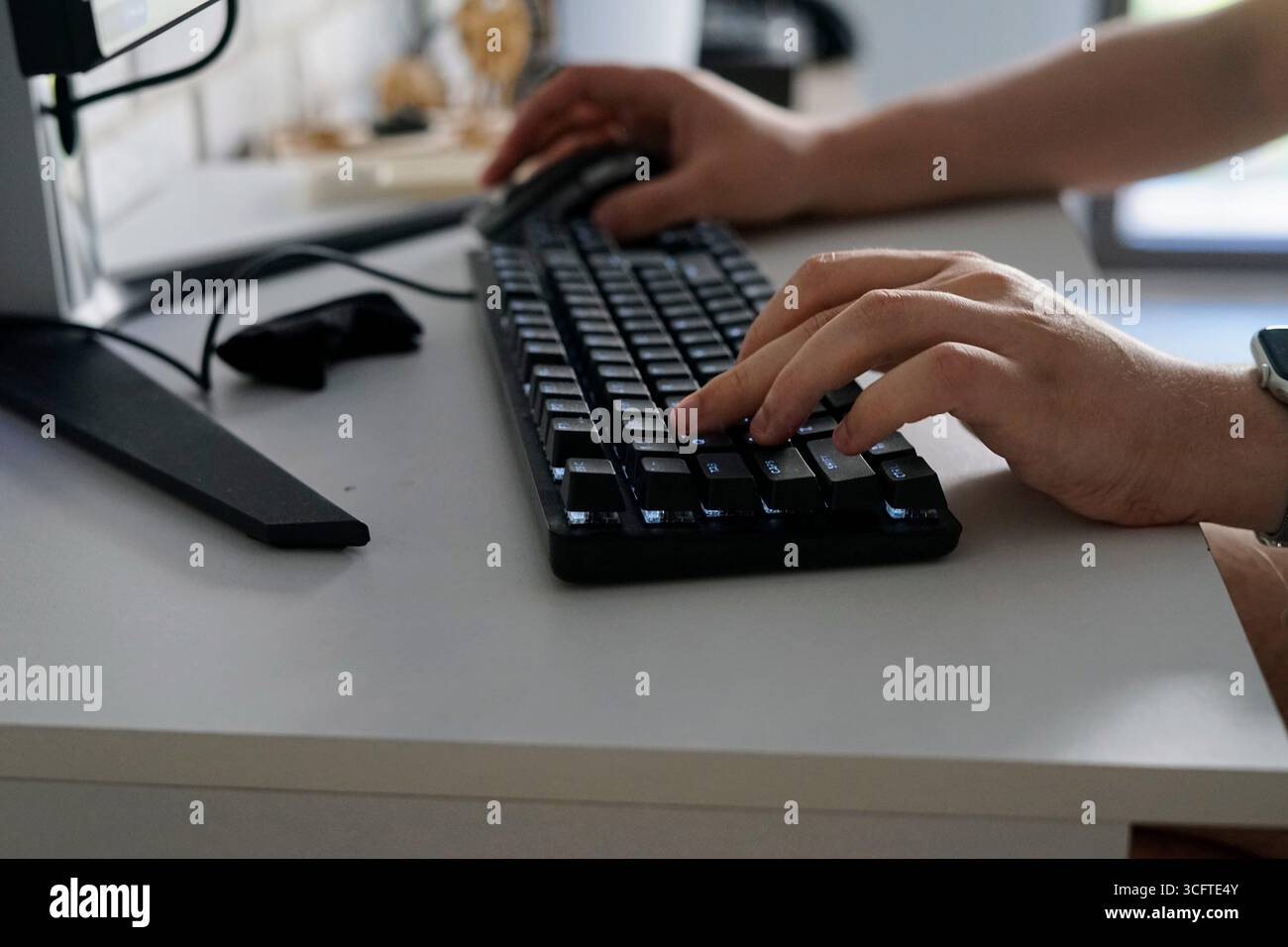 Una vista ravvicinata della digitazione manuale su una tastiera meccanica nera mentre si utilizza un computer con una moderna configurazione della scrivania. Foto Stock