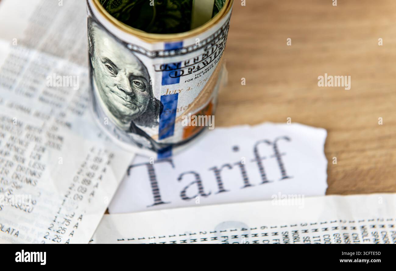 La parola stampata tariffa, la ricevuta del supermercato e un rotolo di dollari USA su un tavolo. Un concetto di inflazione tariffaria, costo della vita. Foto Stock