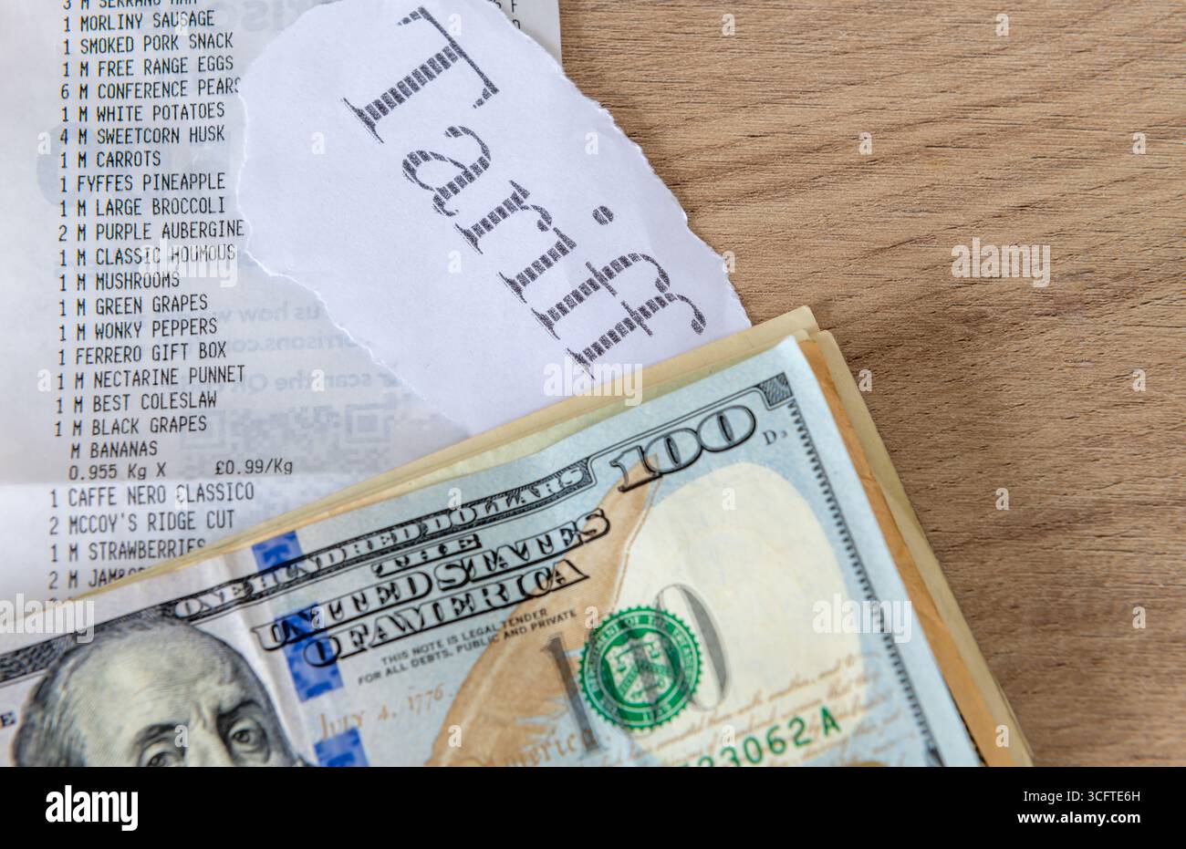 Un mucchio di banconote in dollari USA, la tariffa stampata e una ricevuta del supermercato su un tavolo. Un concetto di costo della vita, inflazione tariffaria. Foto Stock