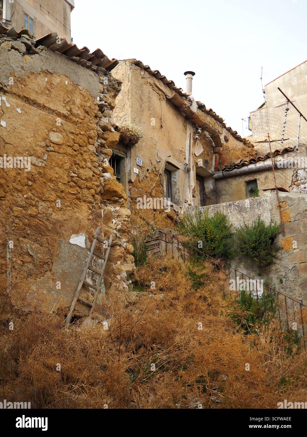 Casa in rovina a Enna con muri in pietra sbriciolati, vegetazione secca, scala rustica e architettura decaduta che mostrano il passaggio del tempo in Sicilia Foto Stock