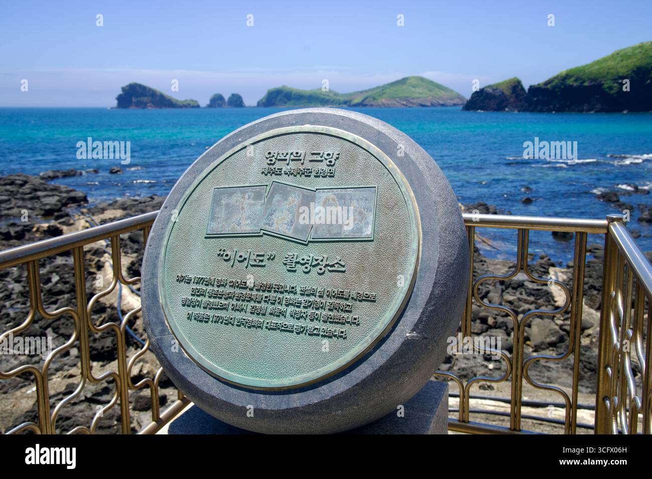 La placca rotonda segna il punto di vista di una location cinematografica a Chagwido, situata sopra piscine di roccia basaltica nera. Gli isolotti al largo punteggiano il mare turchese lungo Jeju Is Foto Stock