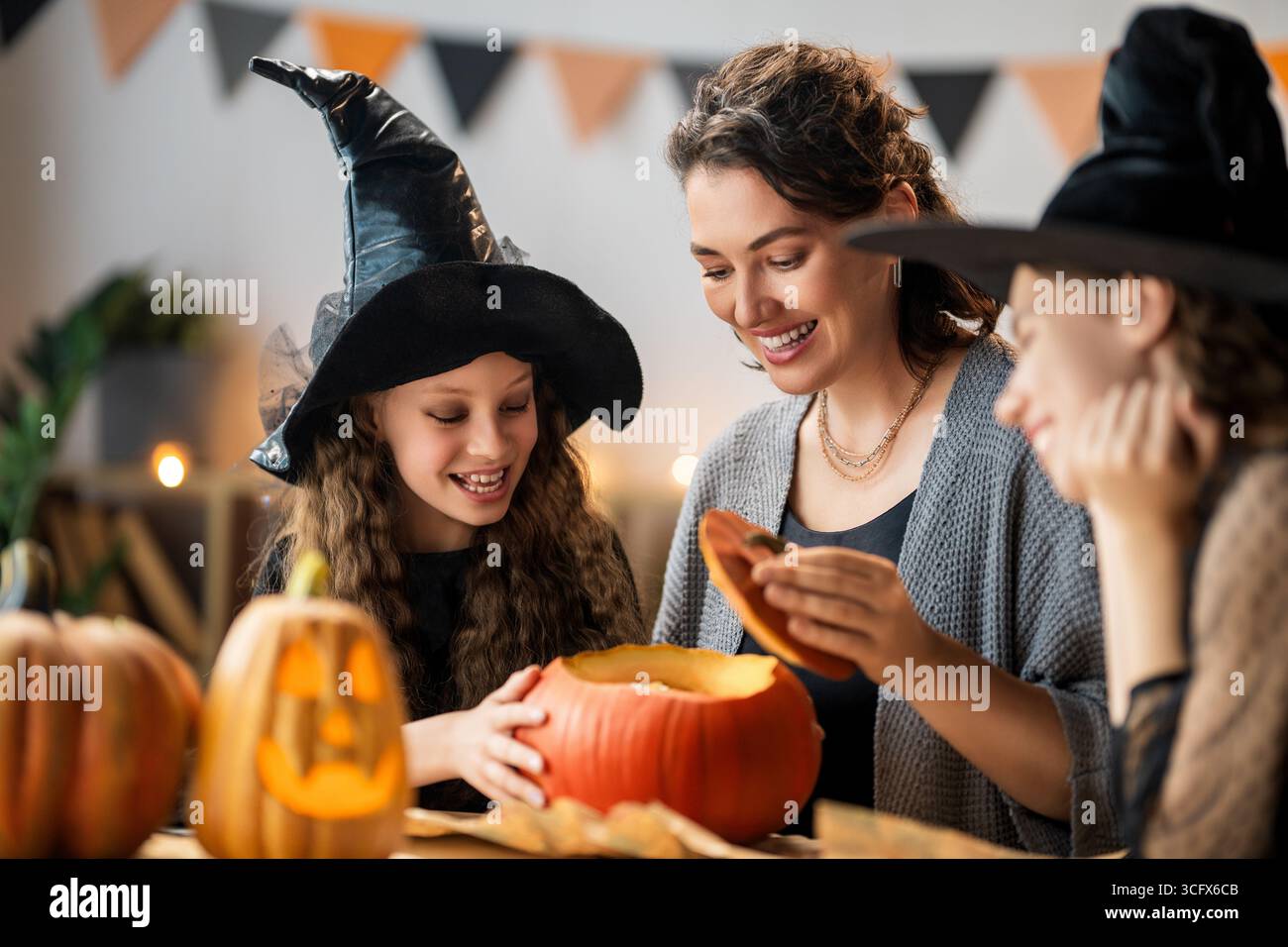 Felice famiglia che si prepara per Halloween. Madre e bambini che intagliano le zucche a casa. Foto Stock