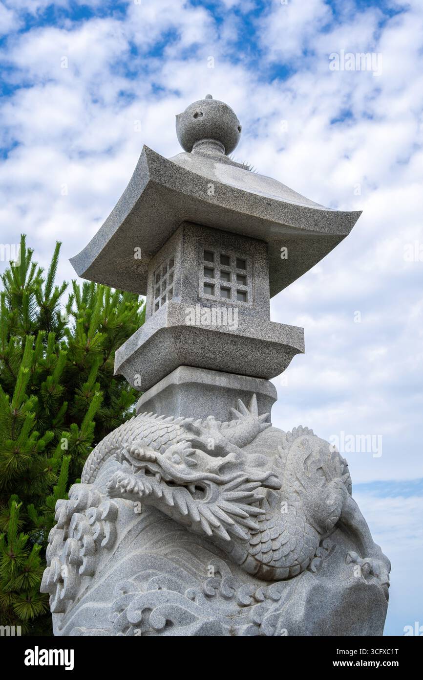 Lanterna in pietra ornata con una scultura di drago si erge sotto un cielo luminoso nell'isola di Enoshima, in Giappone, che mescola arte mitica con il des tradizionale Foto Stock