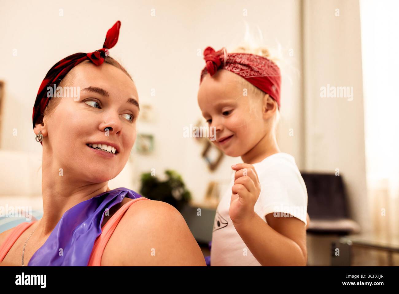 Una madre allegra e suo figlio condividono un momento di gioia insieme all'interno, con un ambiente luminoso. Entrambi indossano bandane rosse corrispondenti, creando una e. Foto Stock