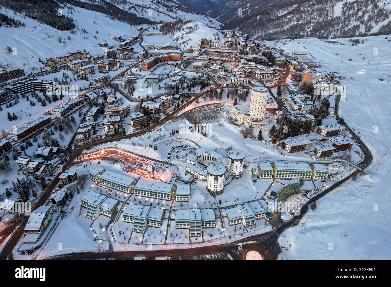 Vista aerea di un villaggio innevato con un'architettura unica, un netto contrasto con il tranquillo paesaggio invernale di Sestriere, Piemonte, Italia. Foto Stock