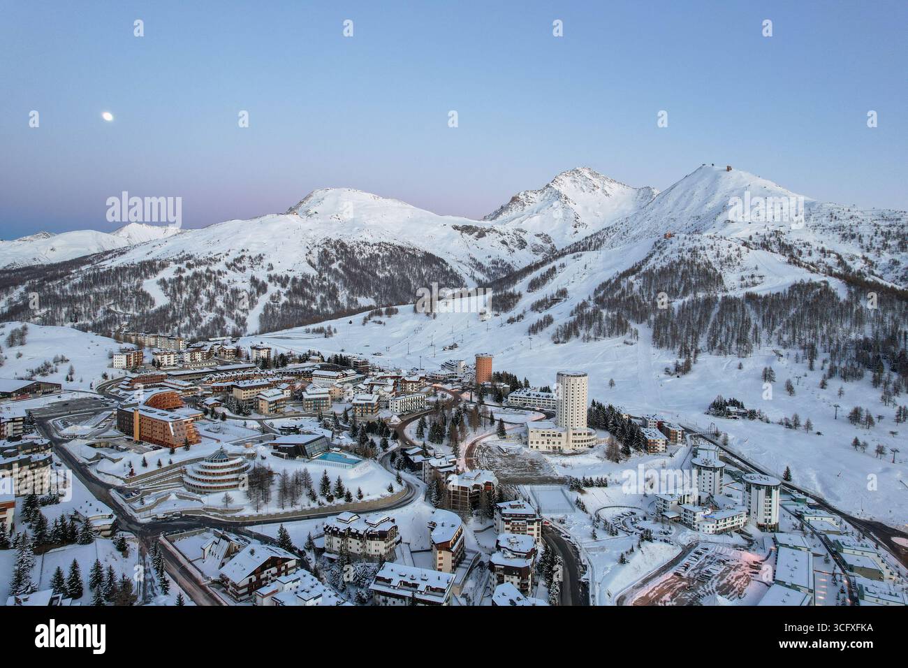 Vista aerea degli edifici innevati annidati tra le maestose montagne innevate, un netto contrasto bianco contro il cielo crepuscolo che svanisce, Sestr Foto Stock