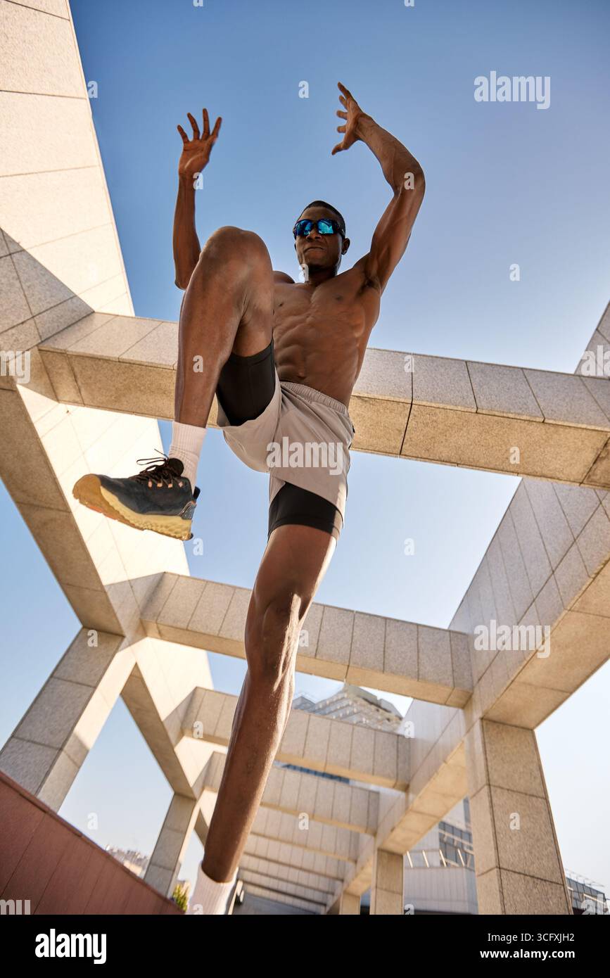 Una dinamica scena urbana caratterizzata da un atleta in forma di azione in mezzo a un'architettura moderna, che mette in mostra forza, movimento ed energia vibrante. T Foto Stock