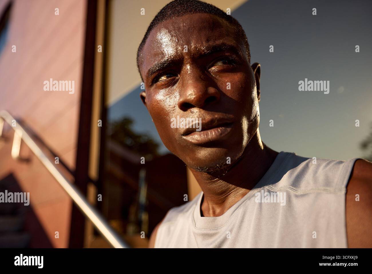 Giovane atletico all'aperto, immerso nel sudore dopo un'intensa sessione di allenamento. La luce dorata del sole al tramonto aggiunge un tono drammatico al suo foc Foto Stock