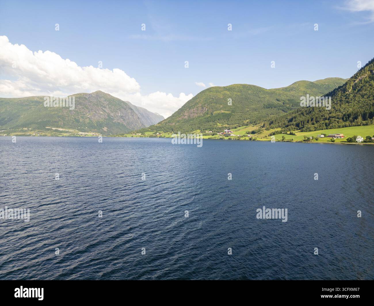 Veduta aerea delle serene e scure acque del lago che incontrano colline verdeggianti sotto un cielo azzurro, Jolstervatn, Sunnfjord, Norvegia. Foto Stock