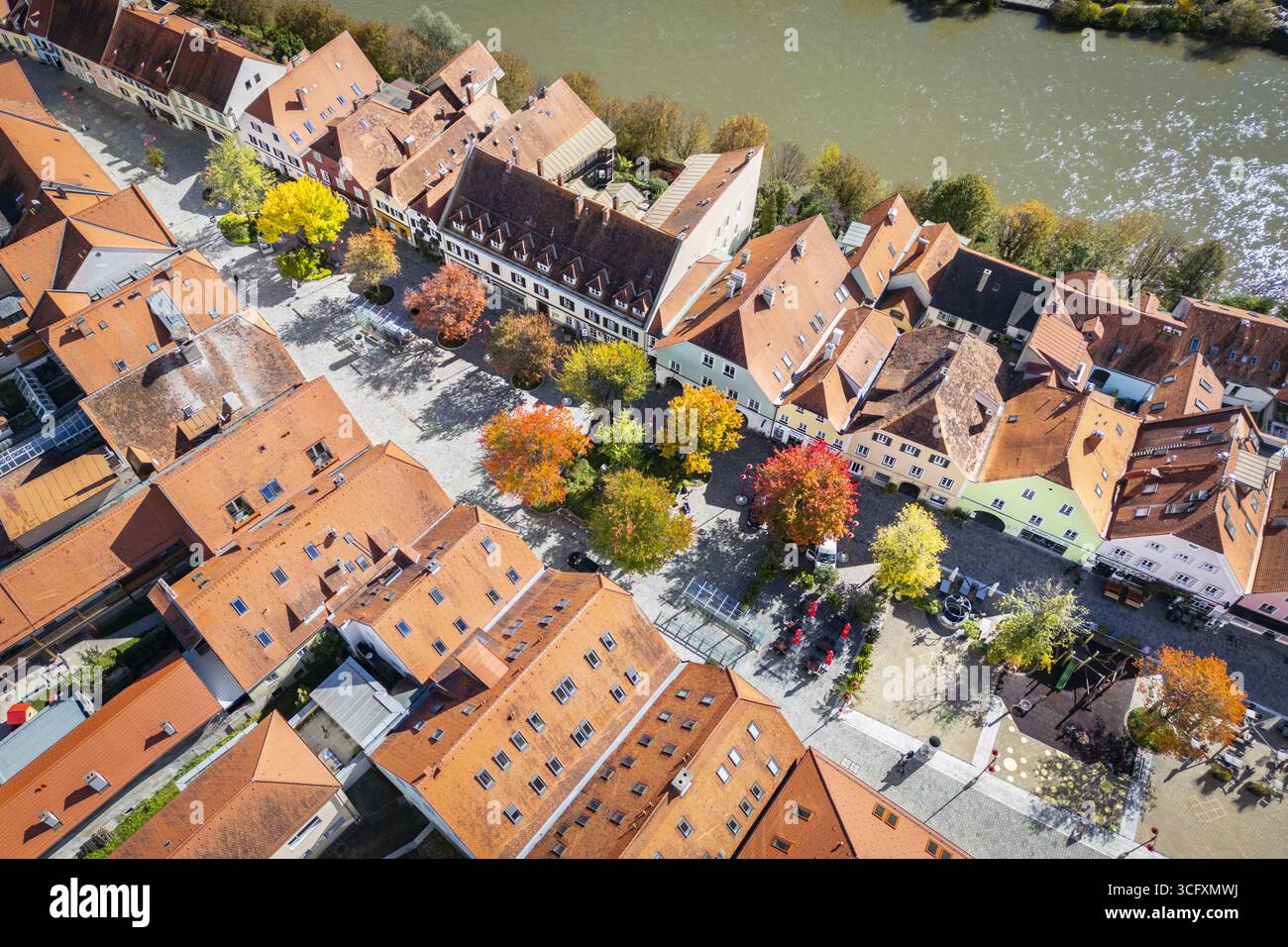 La vista aerea di una pittoresca città si dispiega in un arazzo di tetti in terracotta, vibranti alberi autunnali e il dolce scorrere del fiume Mur, Frohnleiten, Stiria, Austria. Foto Stock