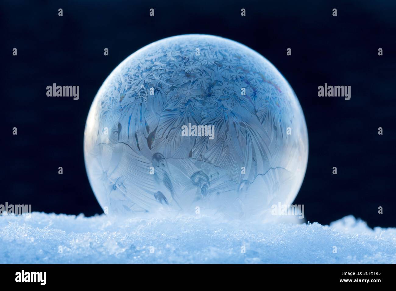 Bolla di sapone congelato sulla neve, magia invernale della bolla di sapone congelato con splendidi cristalli di ghiaccio in una sfera perfetta sulla neve con sfondo sfocato Foto Stock