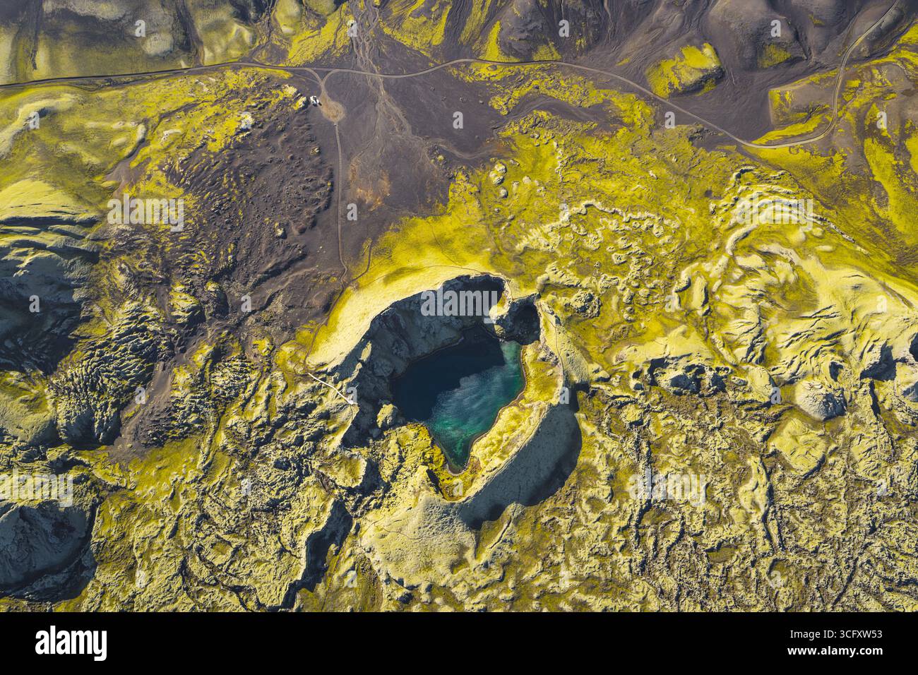 Vista aerea di una piscina turchese nascosta annidata in un paesaggio surreale di muschio giallo vibrante e terra vulcanica scura, che crea un contrasto sorprendente, altopiani, Islanda. Foto Stock