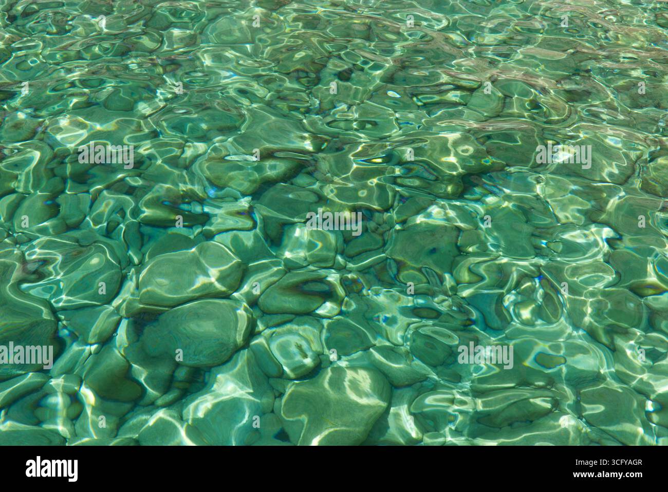 Superficie dell'acqua incontaminata che mostra riflessi della luce del sole su pietre lisce, evocando pace e tranquillità. Foto Stock