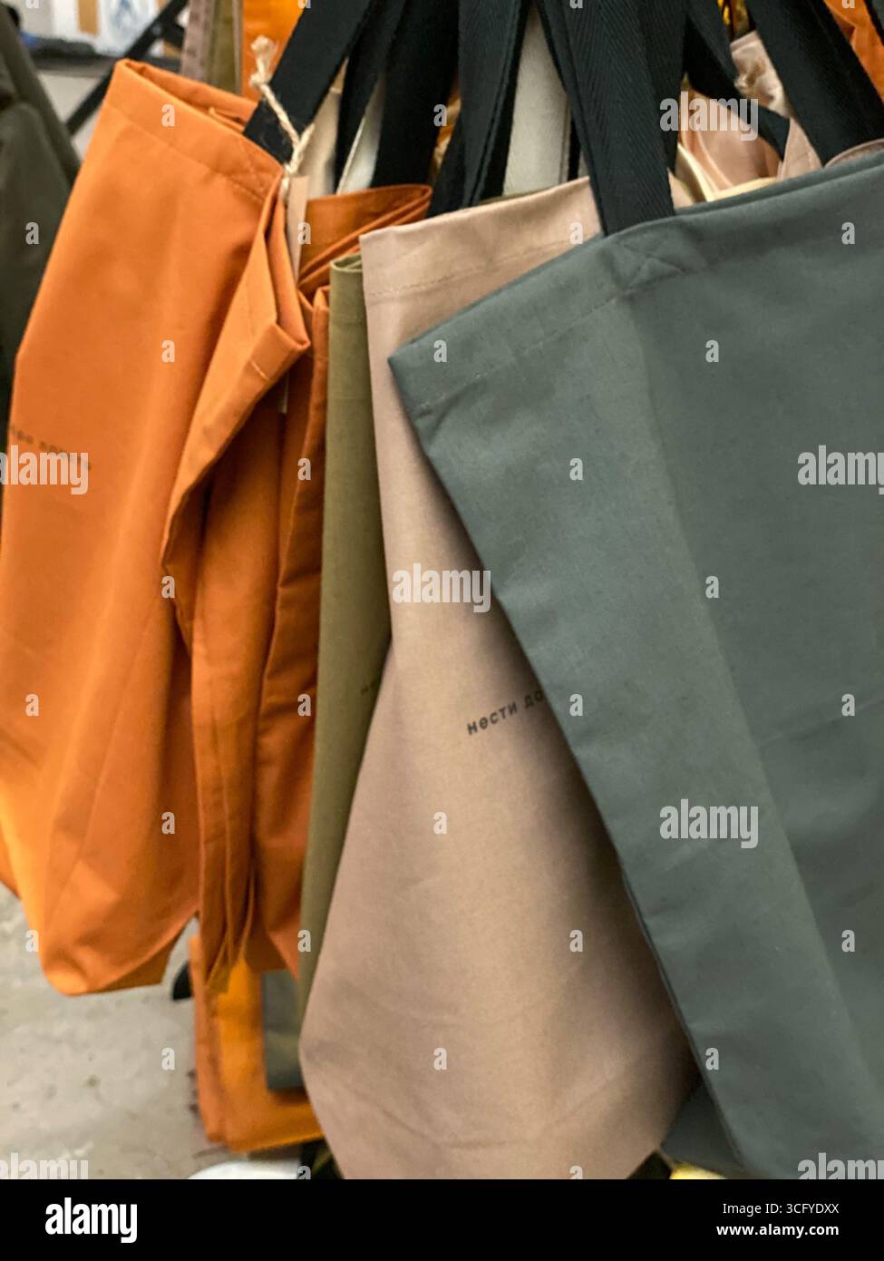 Borse tote colorate riutilizzabili appese in esposizione in un punto vendita, che sottolineano la sostenibilità. Foto mobile Foto Stock