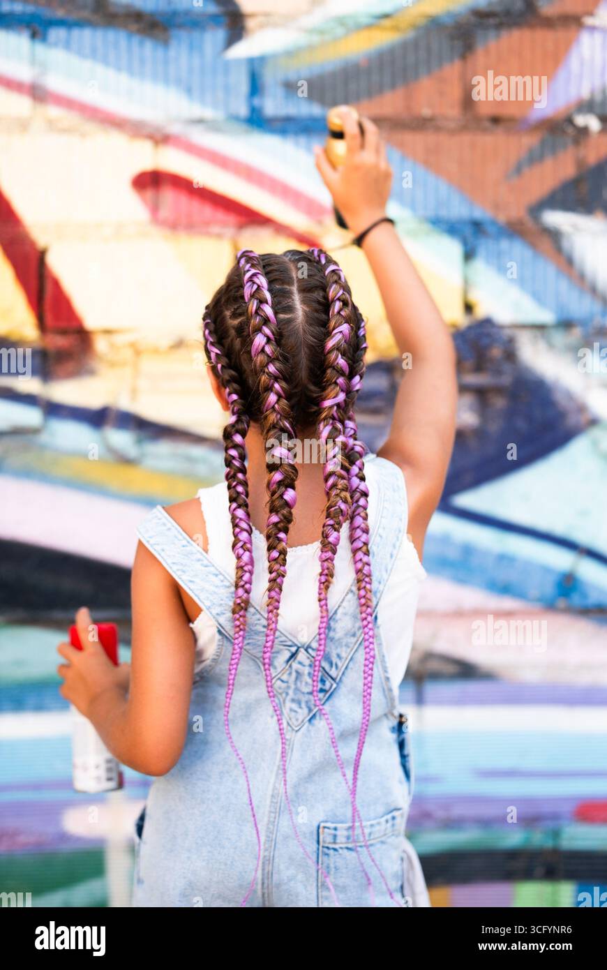 La ragazza con acconciatura intrecciata dipinge un vivace murale sulle mura della città, che mostra talento artistico e creatività Foto Stock