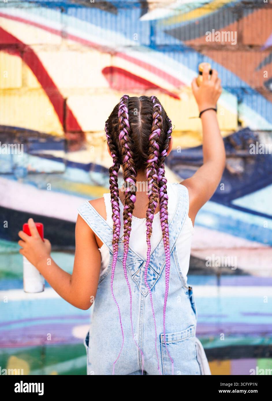 La ragazza con acconciatura intrecciata dipinge un vivace murale sulle mura della città, che mostra talento artistico e creatività Foto Stock