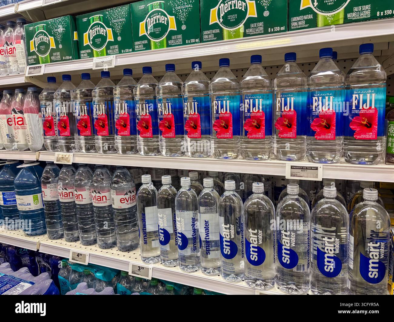 Le bottiglie d'acqua in plastica, tra cui i marchi Fiji, smartwater ed Evian, sono disposte sugli scaffali dei supermercati, evidenziando la prevalenza di materie plastiche monouso e Foto Stock