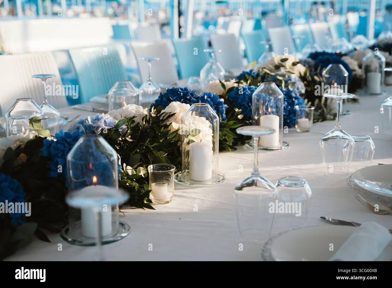 Elegante tavolo per una festa dalle tonalità bianco e blu con candele e composizioni floreali. L'ambiente trasuda un'atmosfera sofisticata perfetta Foto Stock
