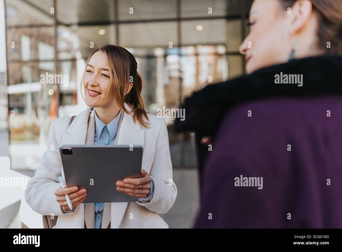 Due donne d'affari che collaborano all'aperto, utilizzano un tablet e si impegnano in una discussione professionale ma accessibile in un ambiente urbano moderno. Foto Stock