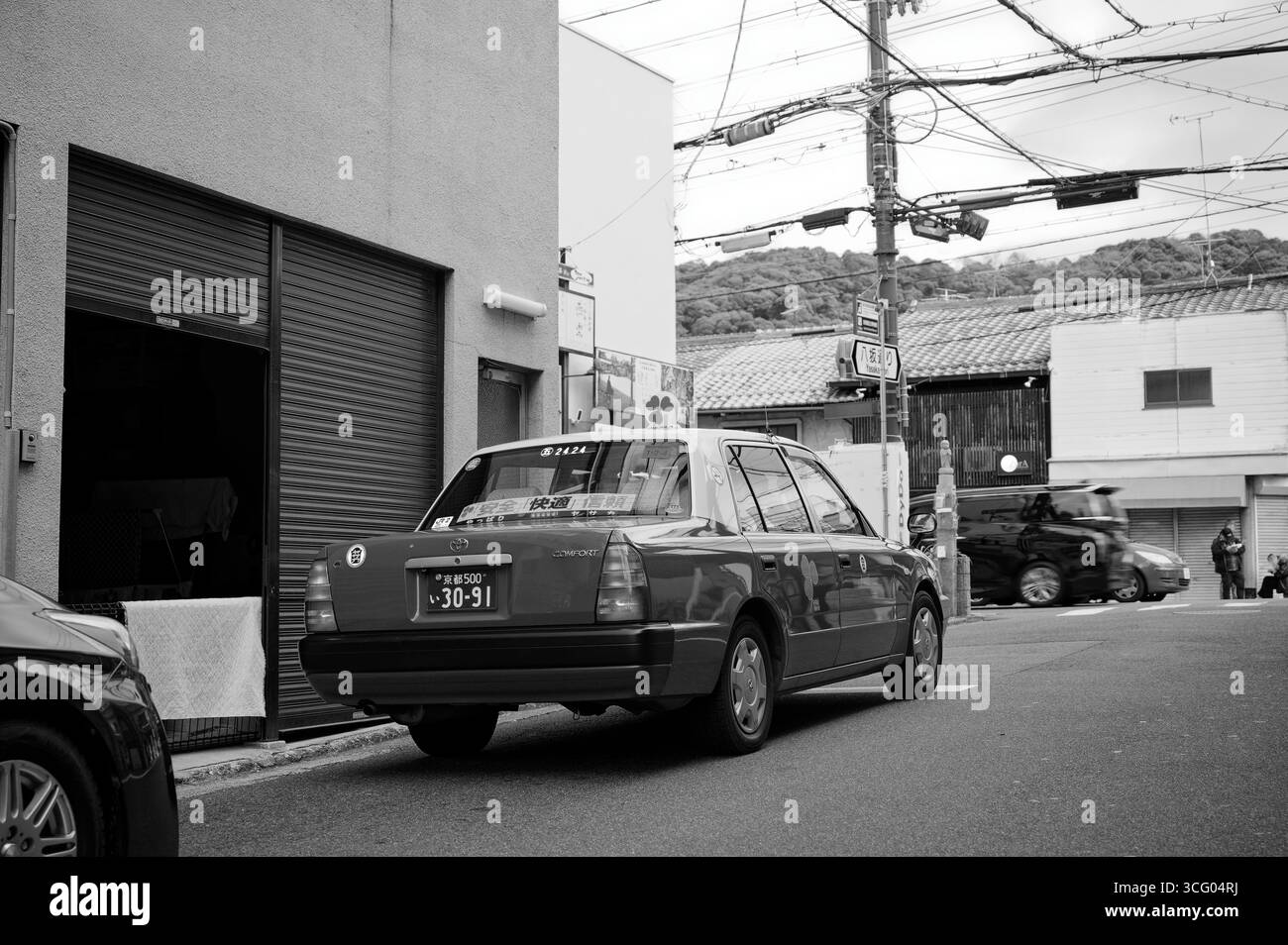 Una scena di strada in bianco e nero a Kyoto con un tradizionale taxi Toyota comfort parcheggiato in una strada tranquilla Foto Stock