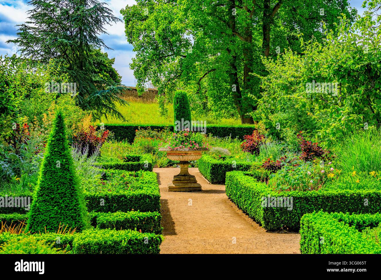 Piantatrice a piedistallo e topiaria estiva colorata all'interno del Bishop's Palace Garden a Wells, Somerset, Inghilterra, Regno Unito Foto Stock