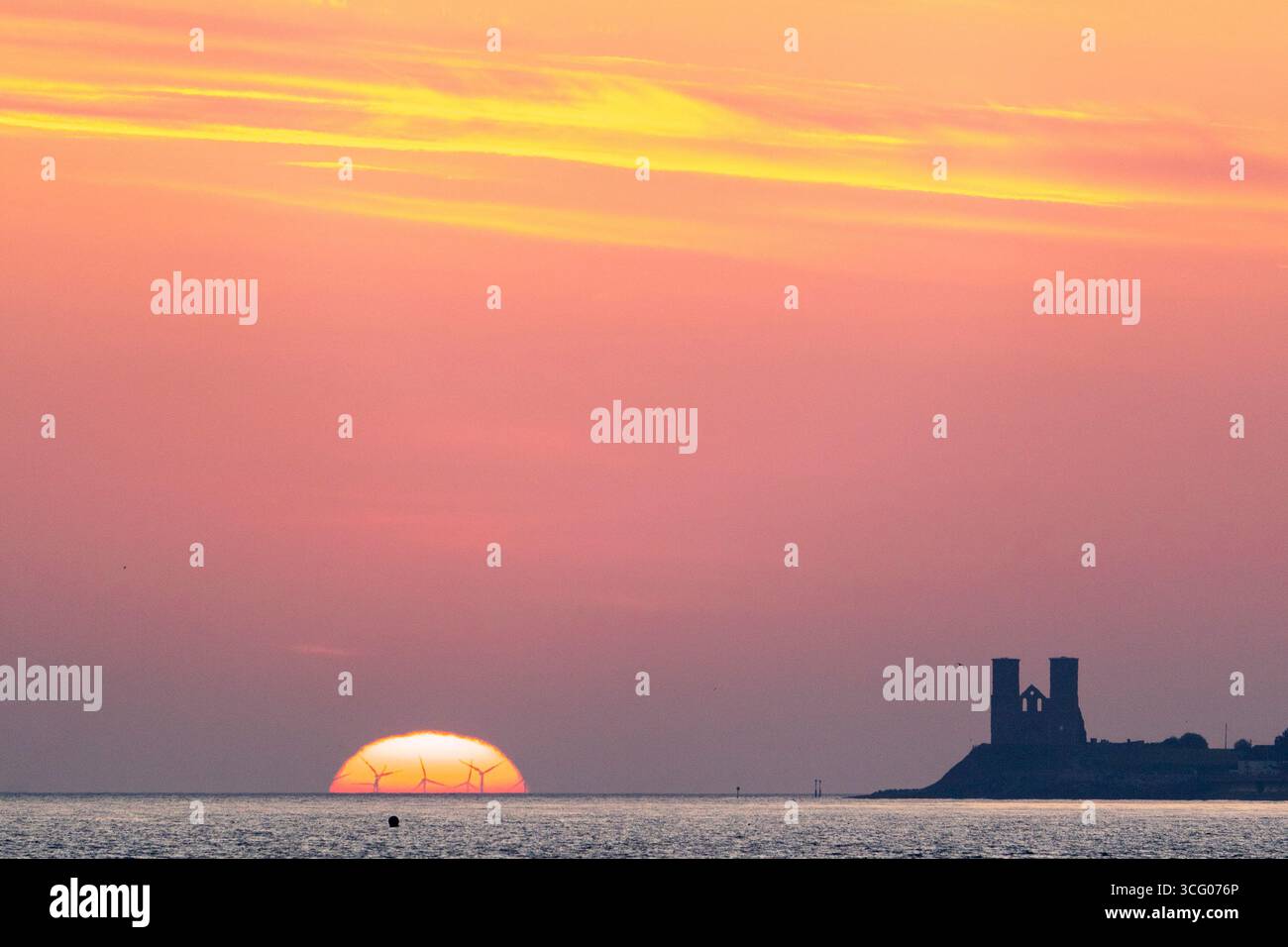 Il sole sorge sul mare e delinea le turbine della Thanet Wind Farm con le torri gemelle della chiesa di Reculver all'orizzonte. Foto Stock