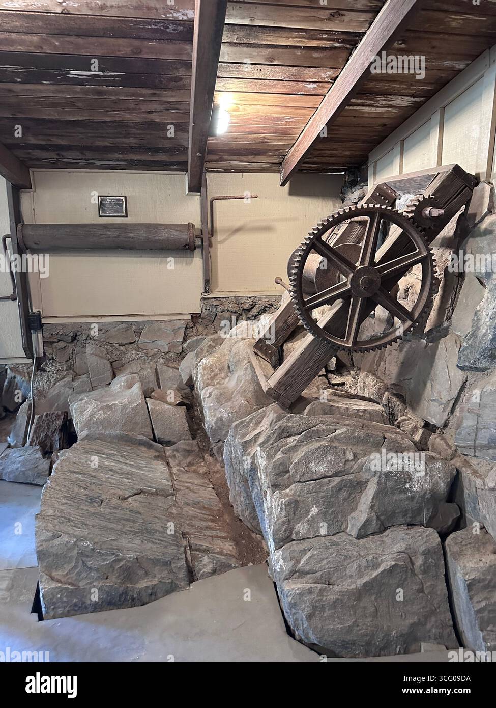 Ingranaggi di macchinari storici per l'estrazione mineraria incorporati nella roccia all'interno di una struttura conservata - Immagine stock catturata con smartphone