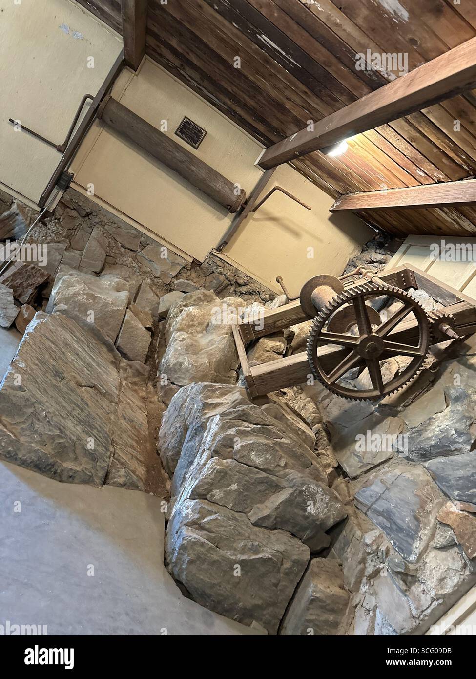 Ingranaggi di macchinari storici per l'estrazione mineraria incorporati nella roccia all'interno di una struttura conservata - Immagine stock catturata con smartphone