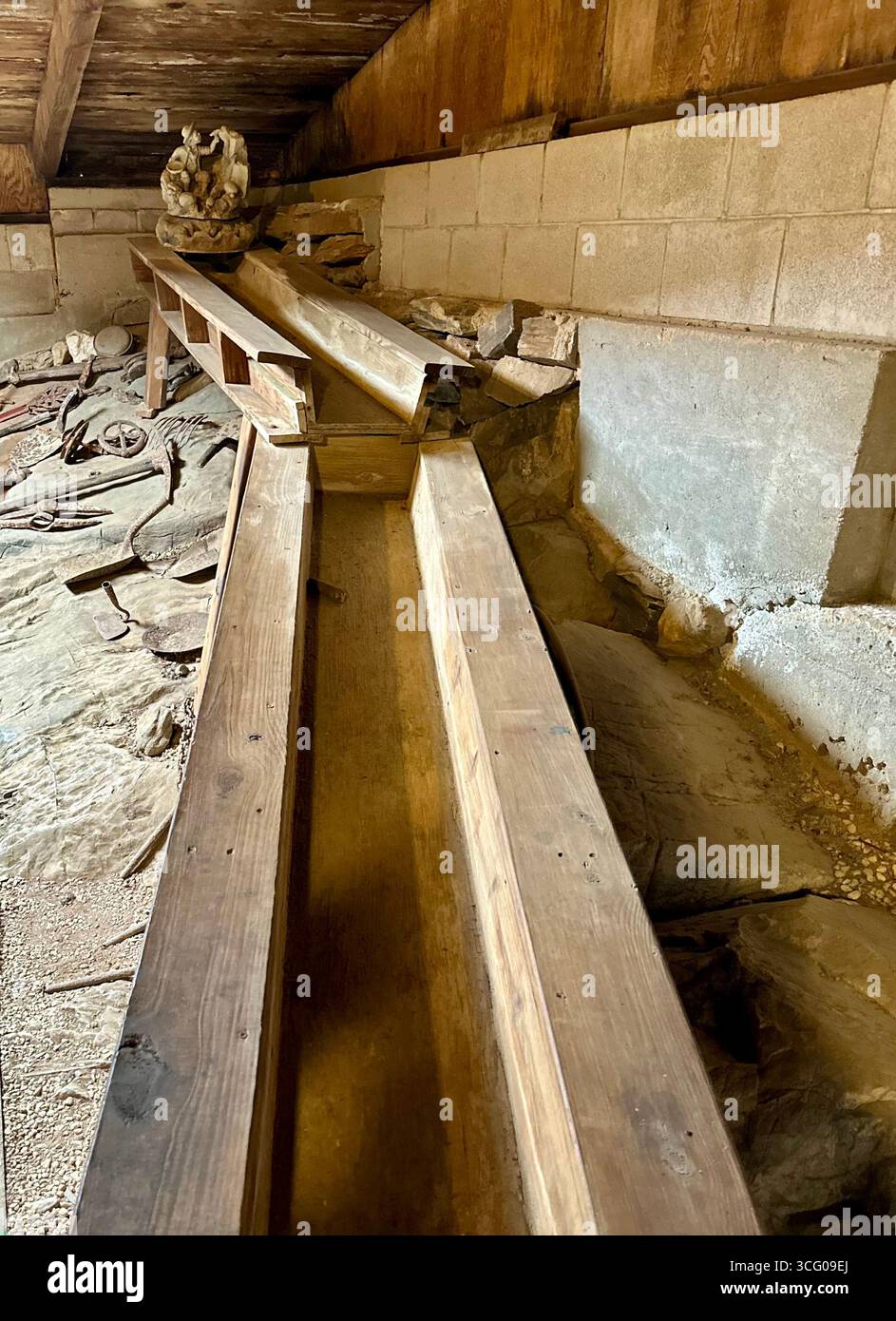 Una calice di legno intemprata o una vasca d'acqua all'interno di una storica struttura mineraria, circondata da antichi utensili e lavori in pietra. - Immagine stock catturata con smartphone
