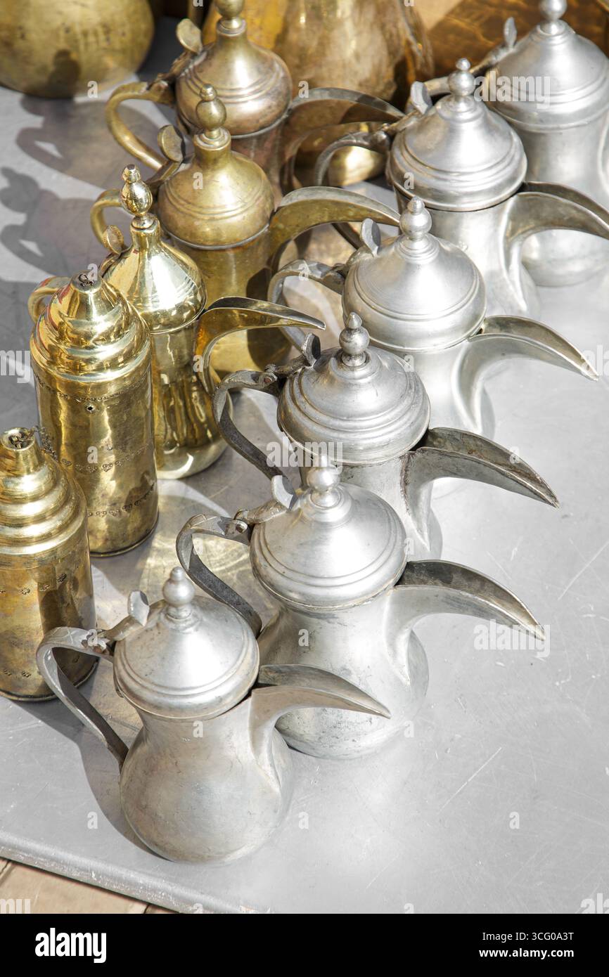 Caffettiere d'epoca arabe dallah in ottone e alluminio, usate e intemperie, esposte in vendita in un mercato delle pulci in Arabia Saudita. Foto Stock