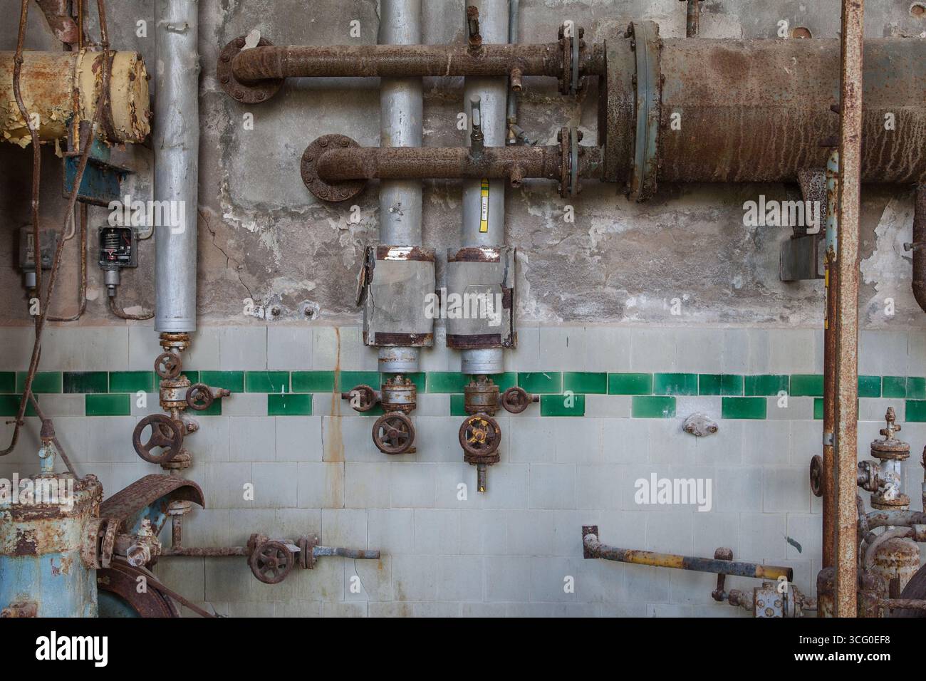 In una sala attrezzature abbandonata, è visibile un vecchio sistema di tubazioni. I tubi, le valvole e i condotti arrugginiti mostrano decadimento e disuso a lungo termine, riflettendo il bui Foto Stock